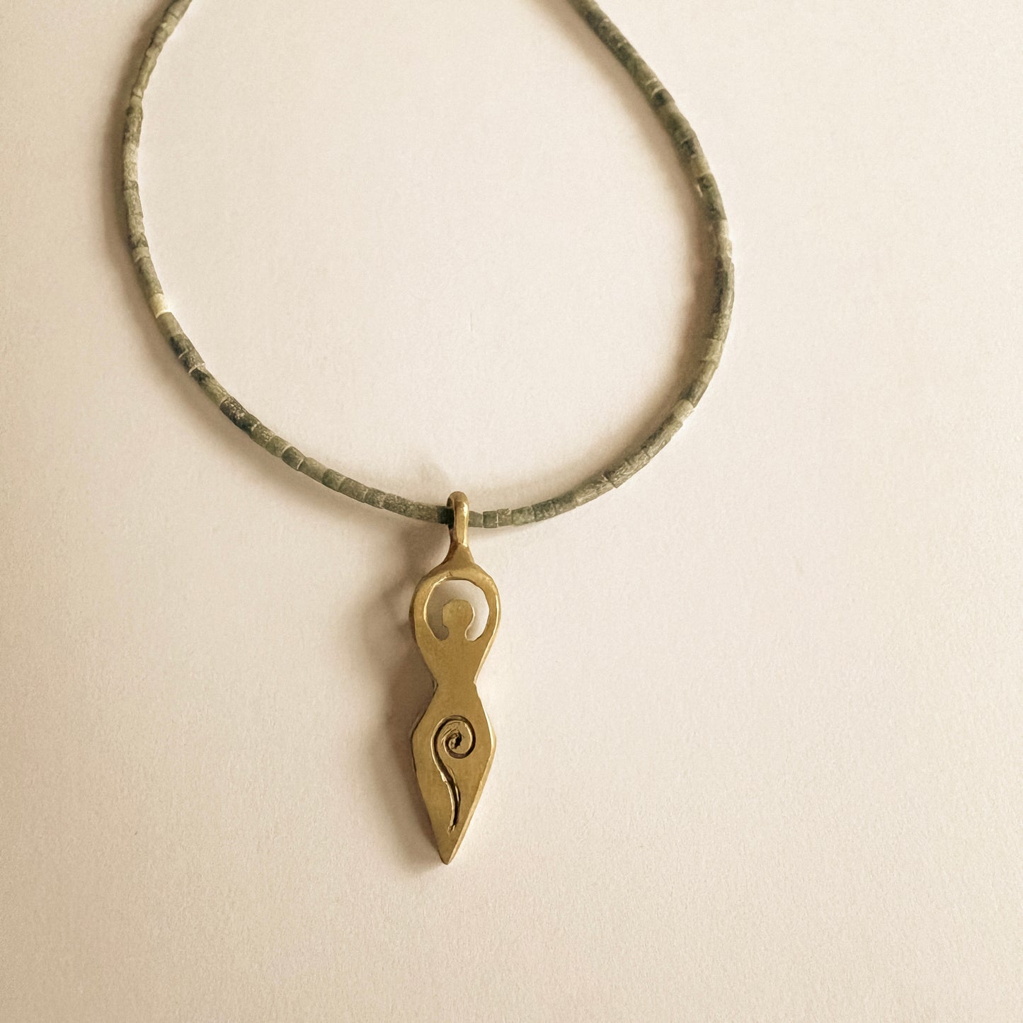 Close-up of a feminine symbol pendant necklace in brass with fine jade necklace
