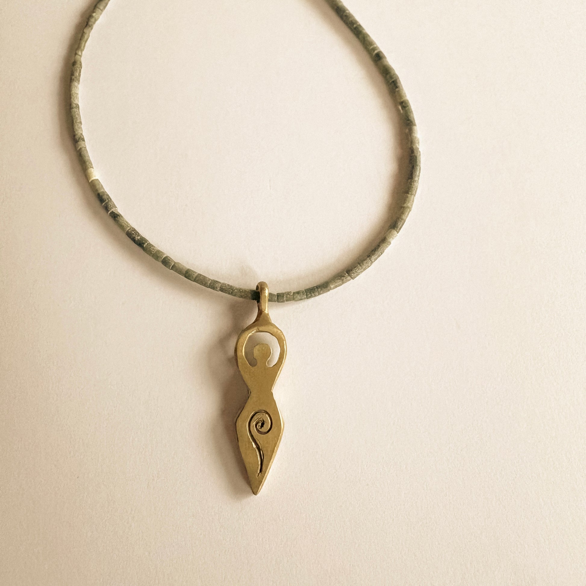 Close-up of a feminine symbol pendant necklace in brass with fine jade necklace