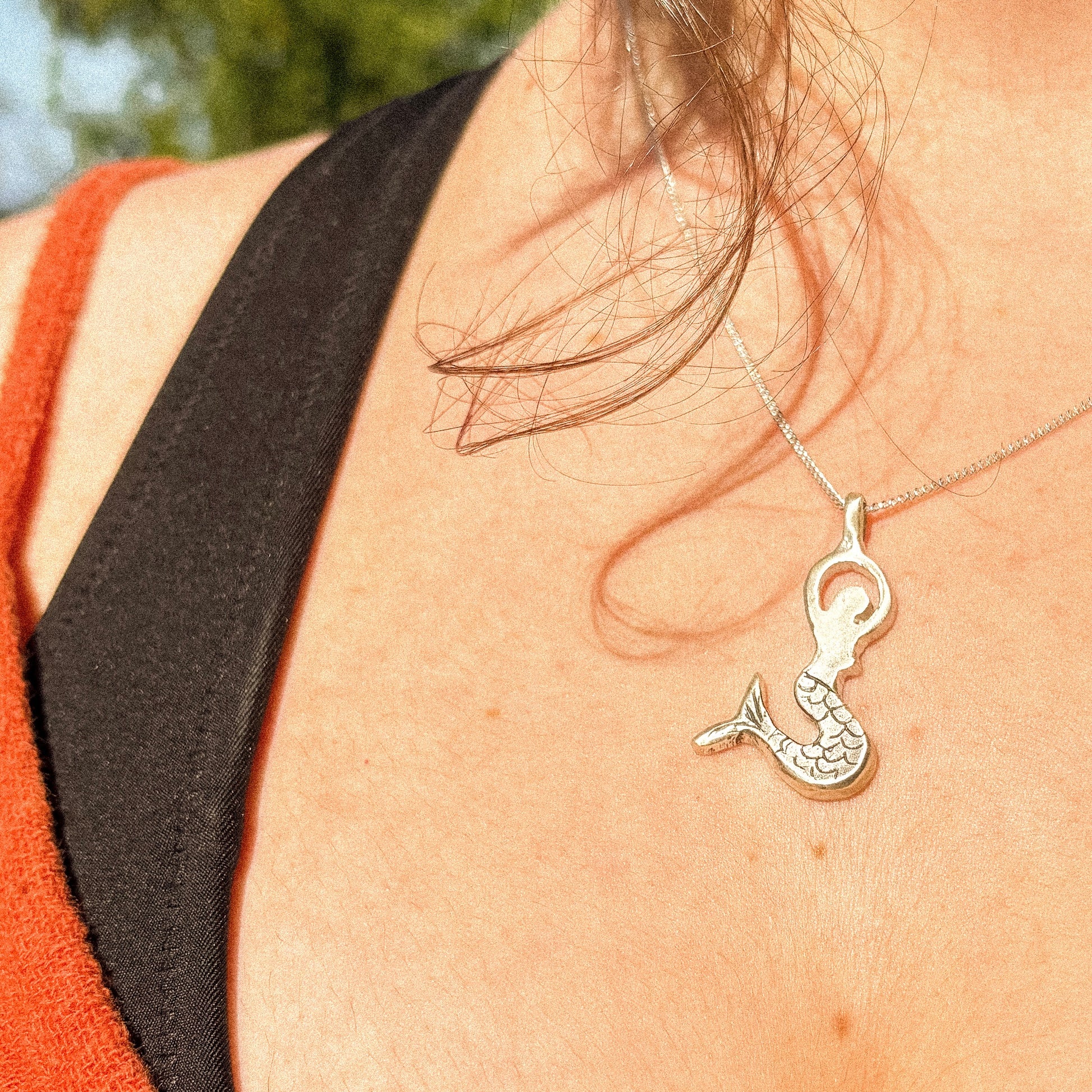 Silver mermaid tail necklace worn by a person close-up