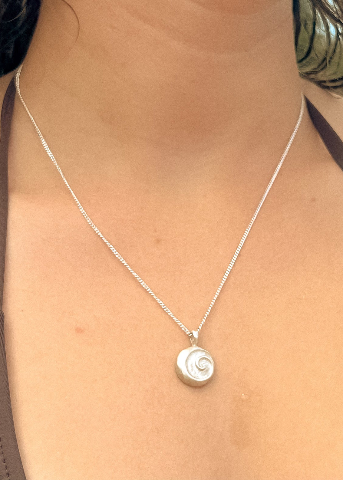 A close-up image of a person wearing a silver pendant necklace with a spiral design at the center, part of the Anahata series.