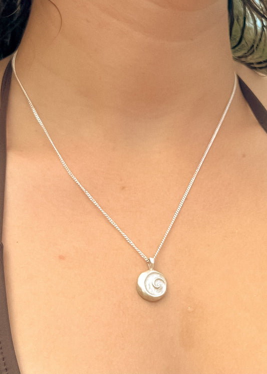 A close-up image of a person wearing a silver pendant necklace with a spiral design at the center, part of the Anahata series.