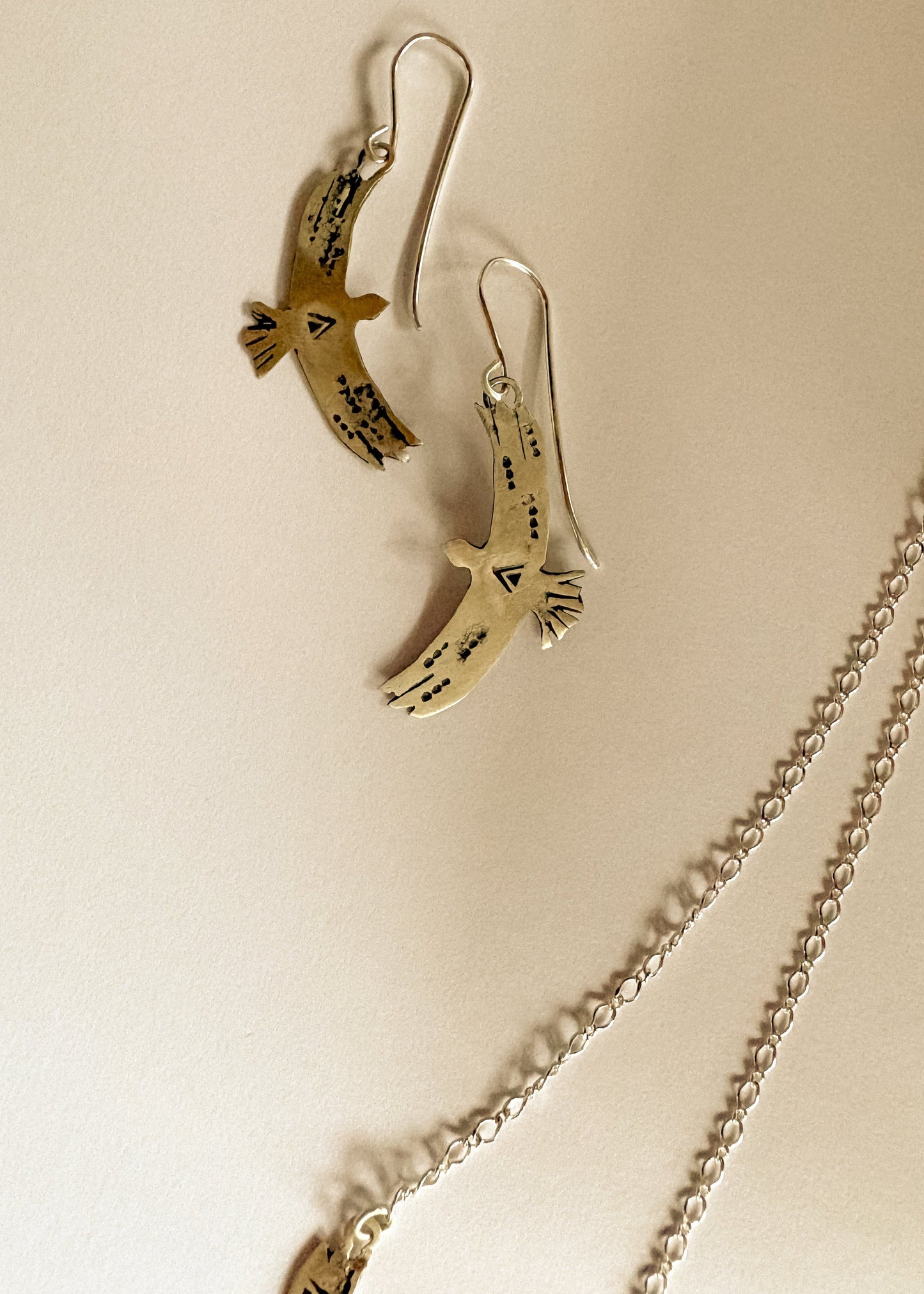 Silver bird-shaped earrings and a silver chain on a beige background
