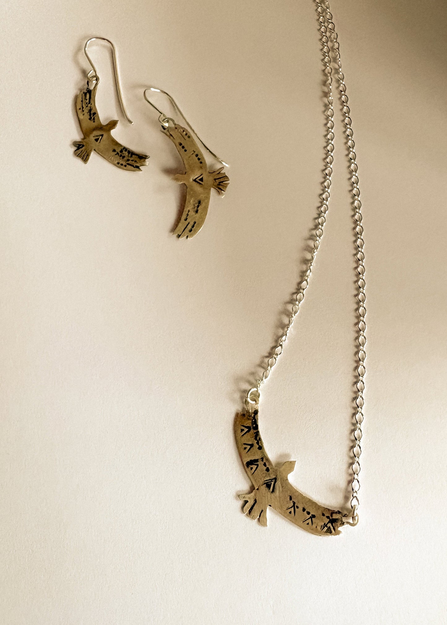 Silver bird-shaped earrings and necklace on a beige background