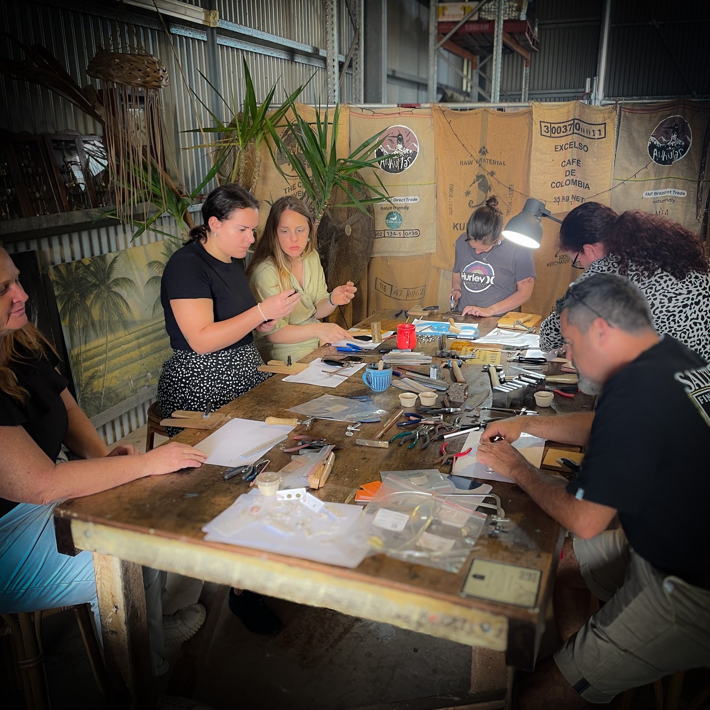 A group of people participating in a jewelry making workshop, sitting around a table with tools and materials, working on creating stacker rings.