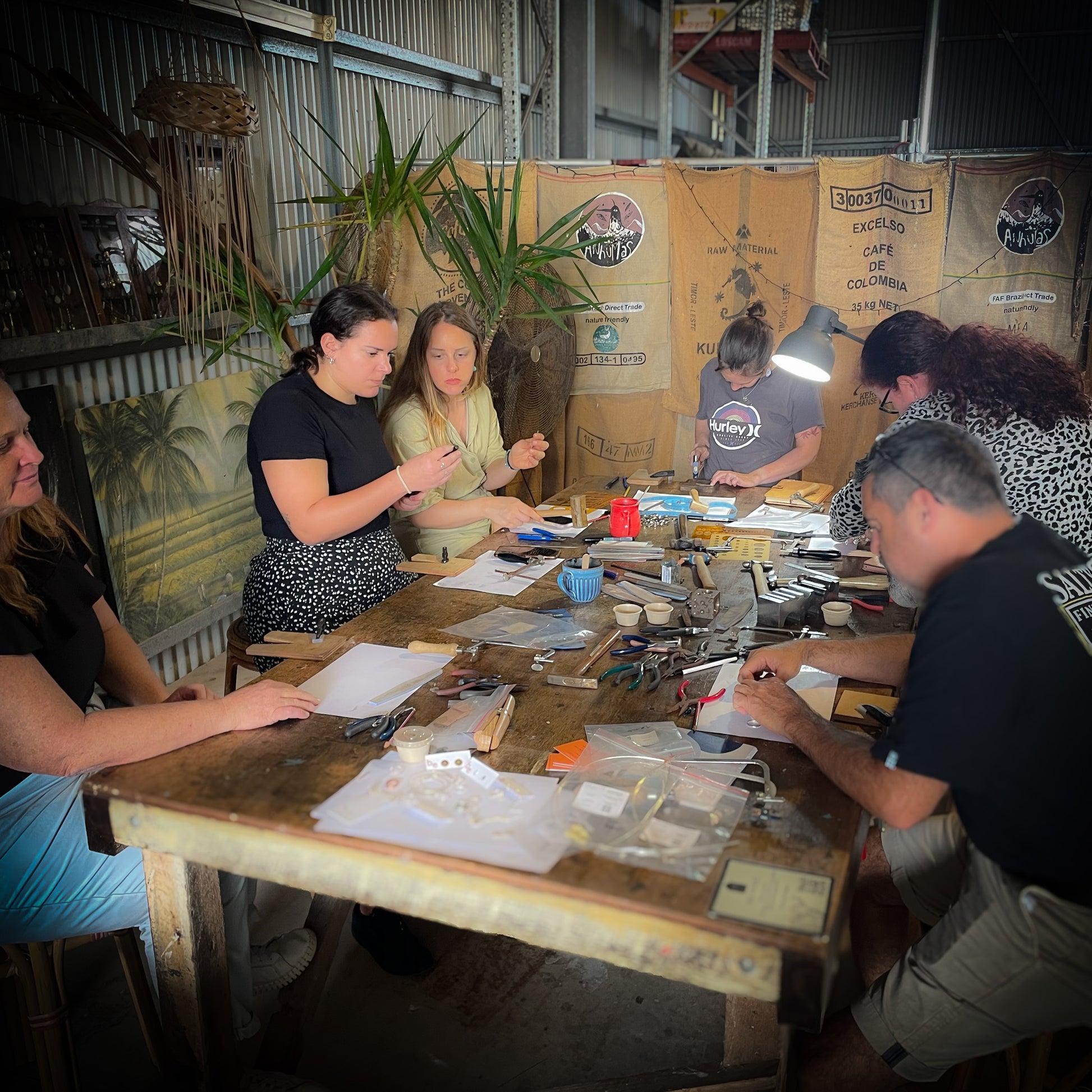 A group of people participating in a jewelry making workshop, sitting around a table with tools and materials, working on creating stacker rings.