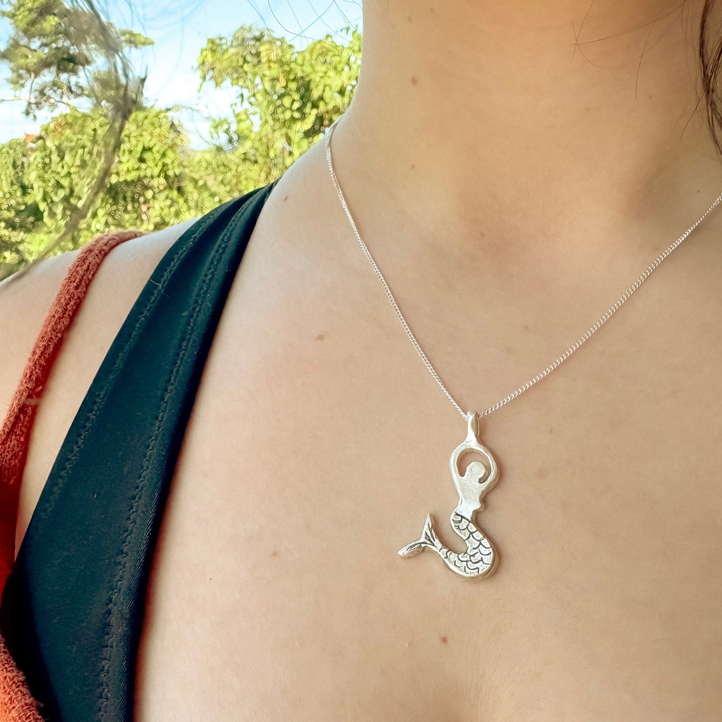 Silver mermaid pendant necklace on a person with a blurred natural background