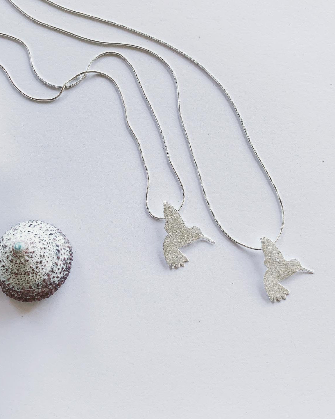 Silver necklace with bird pendants on a light gray background