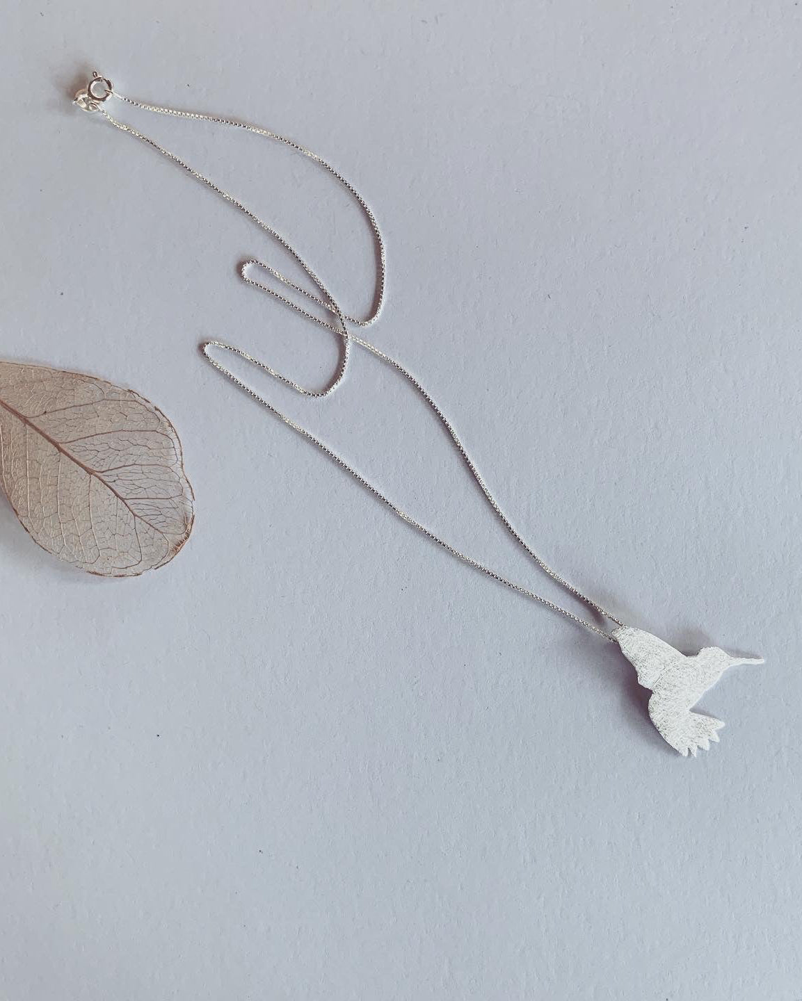 Silver necklace with a bird-shaped pendant on a light gray background