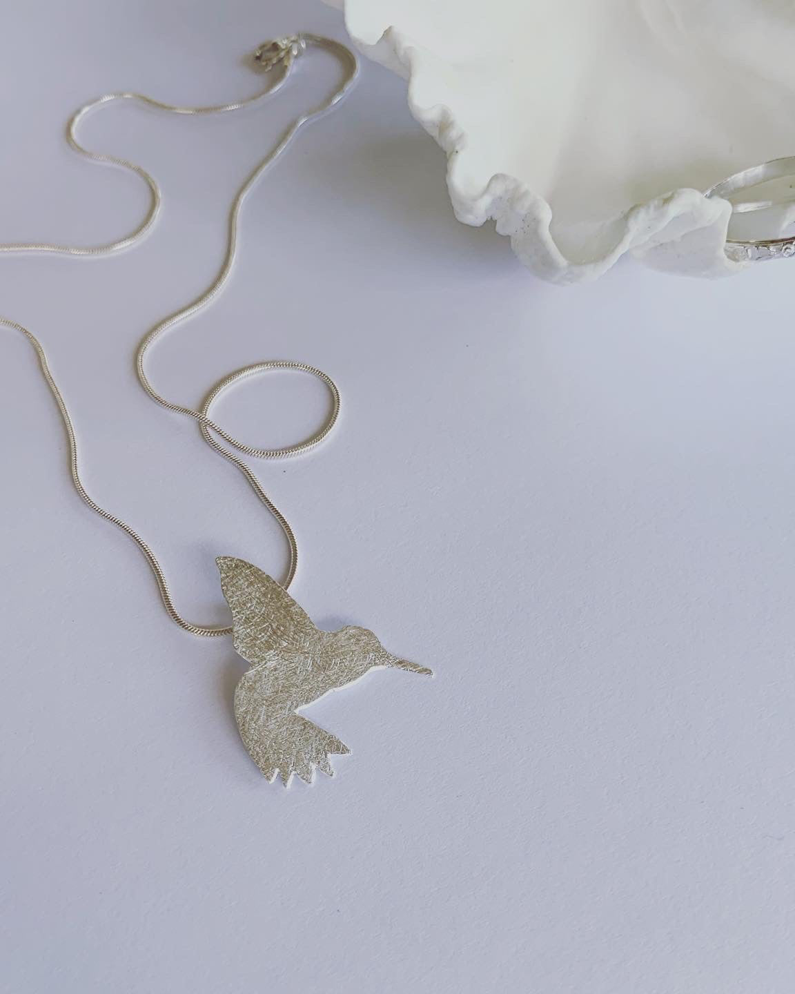 A silver pendant necklace featuring a stylized sunbird design against a white background.